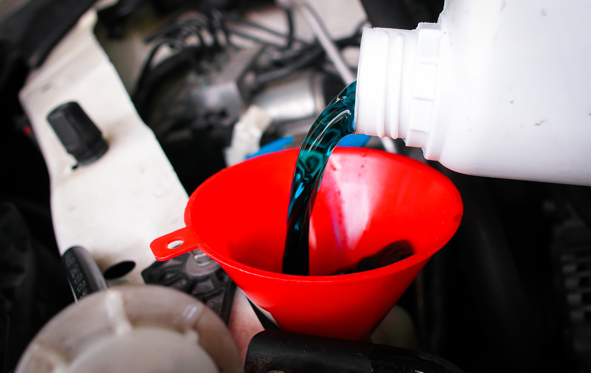 Pouring dark liquid into a red funnel in an engine bay