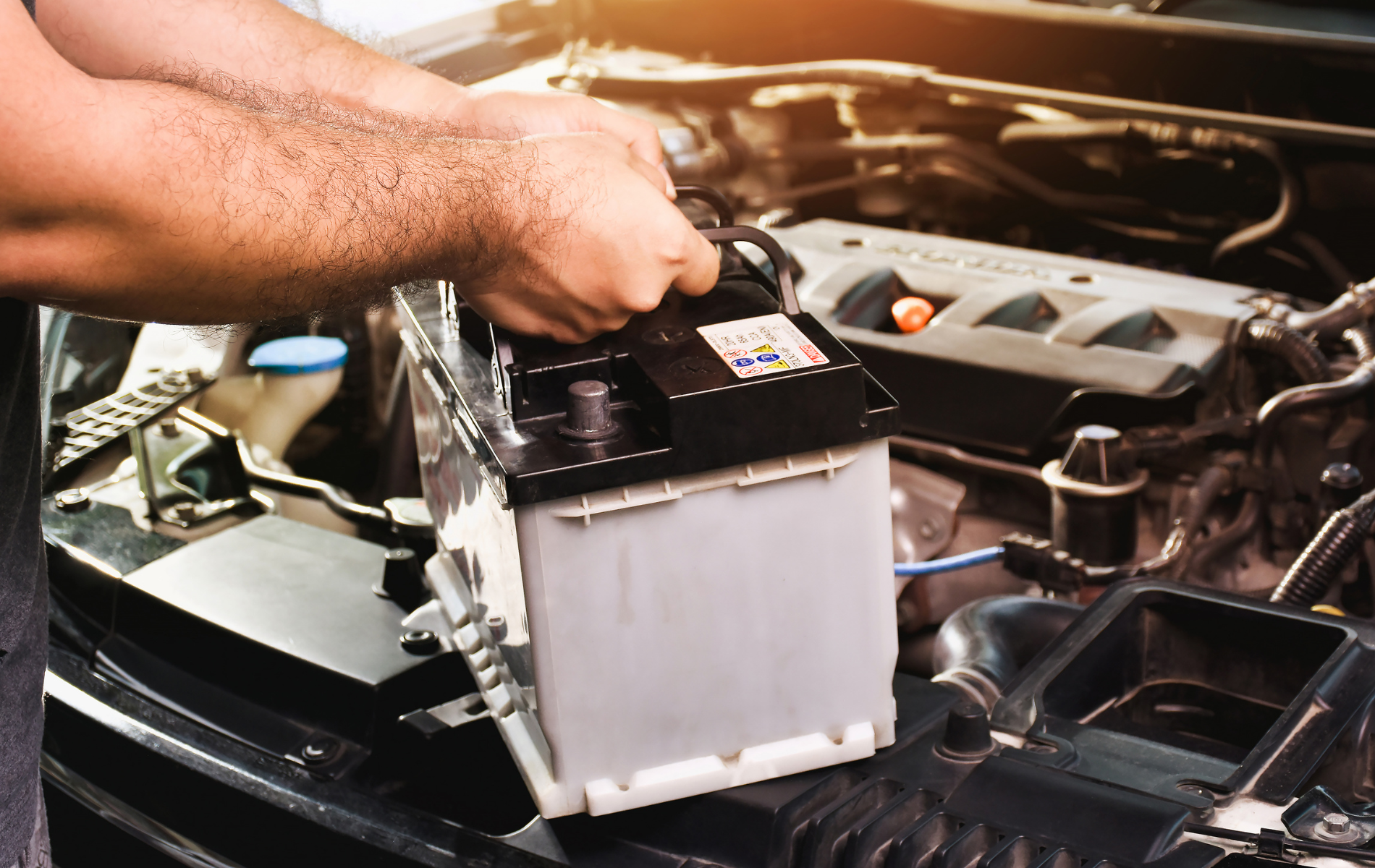 Person installing a car battery in an open engine bay