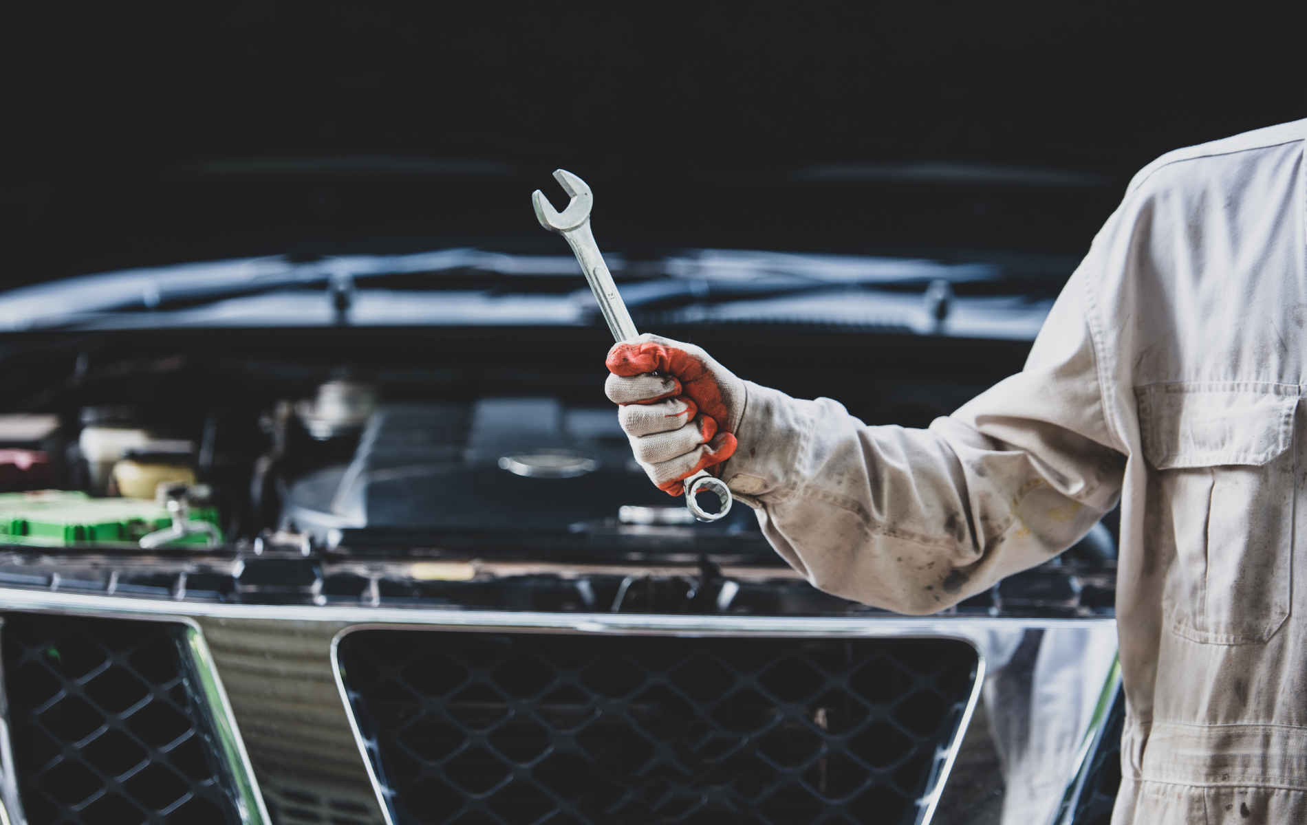 Mechanic holding a wrench in front of a car with its hood open