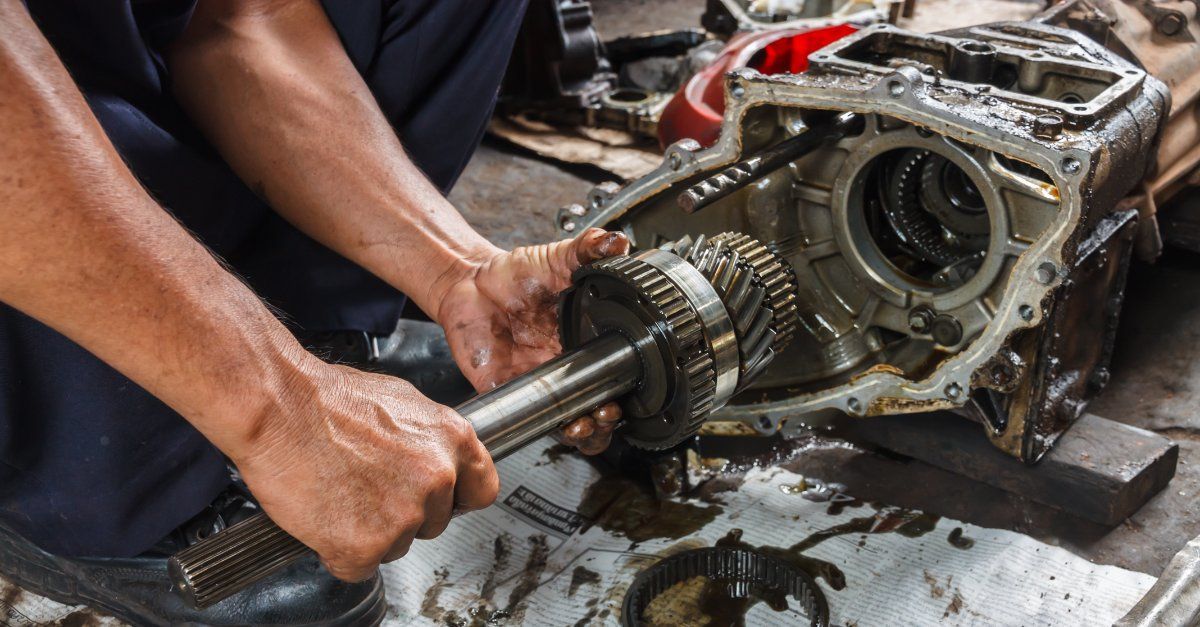 Hands using a tool to remove a gearbox transmission in a greasy workshop.