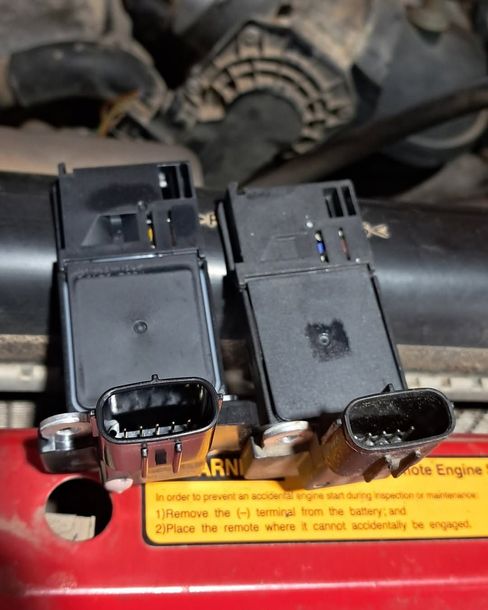 Two black electrical connectors on a red engine part with a yellow warning label