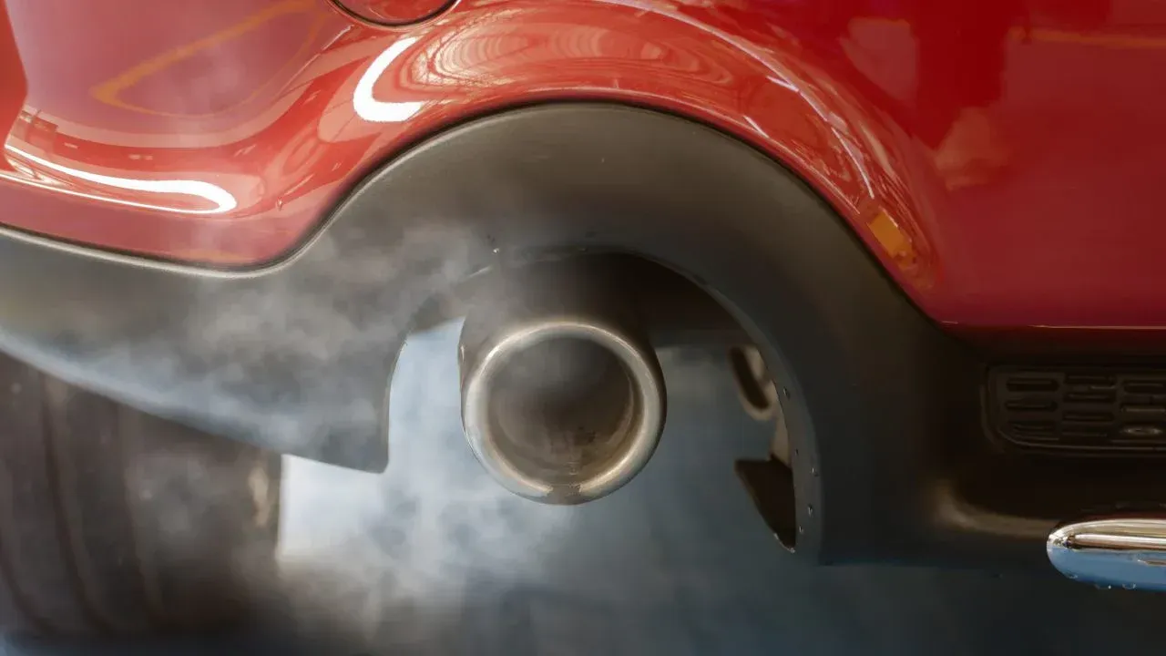 Close-up of a red car’s exhaust pipe with smoke drifting out