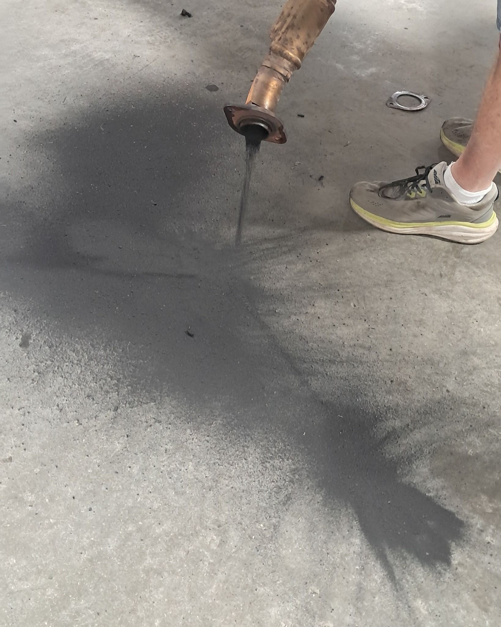 Worker using a hose to spray water onto a concrete pavement, with a sneakered foot visible nearby.