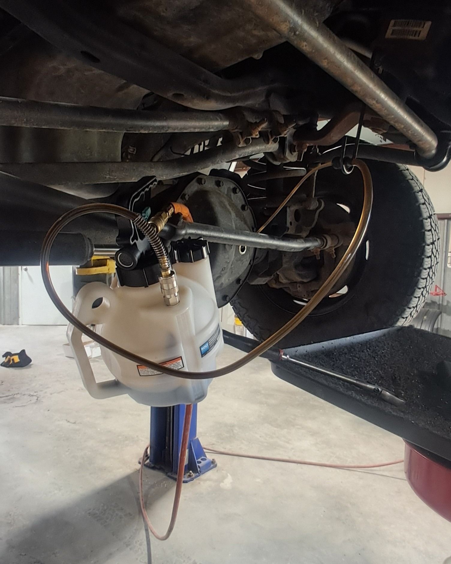 Vehicle undercarriage with a blue jack and white fluid reservoir in a garage