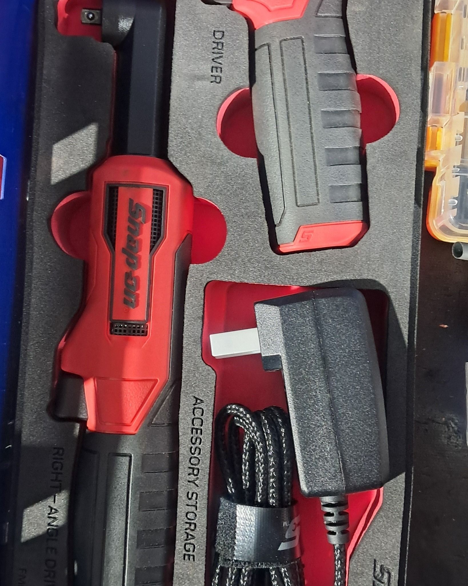 Red and gray utility knife set in a black foam tool case with a black cable and yellow-handled tool.