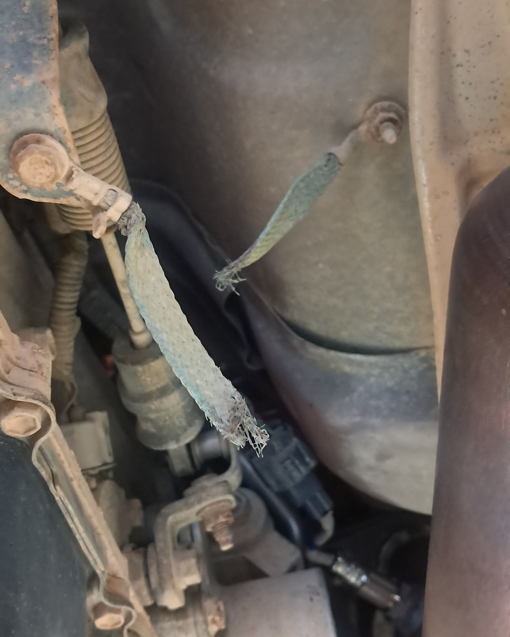 Close-up of a vehicle underside with frayed fabric straps and metal components near a wheel well