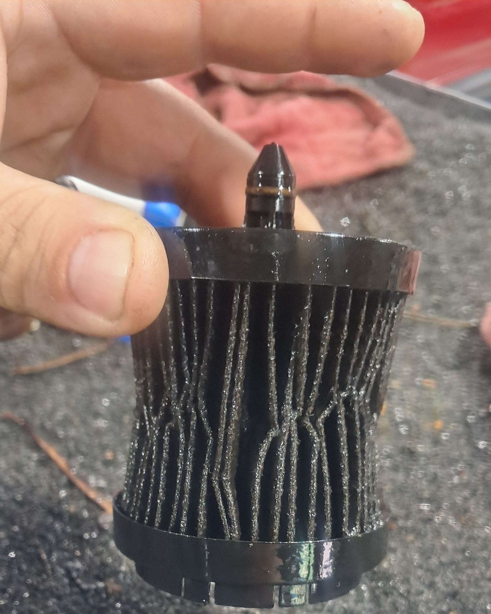 Close-up of a small black cylindrical filter cartridge being held between fingers.