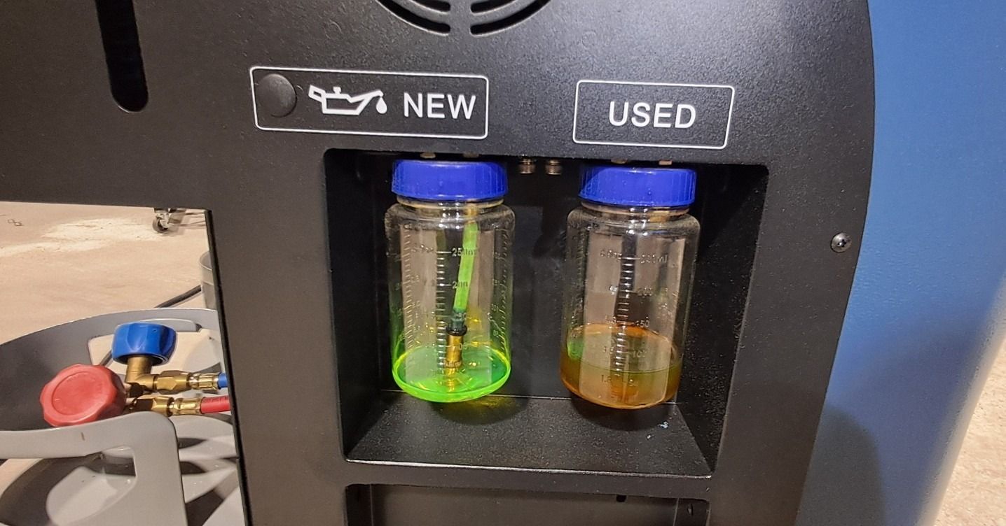 Two plastic sample jars in a black display, labeled NEW and USED, with blue lids and colored liquid inside