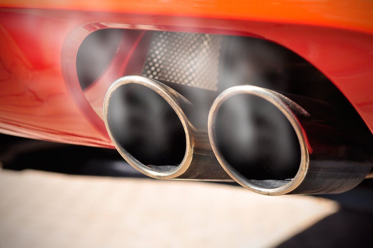 Close-up of dual chrome exhaust pipes on a red car, with motion blur and heat haze.