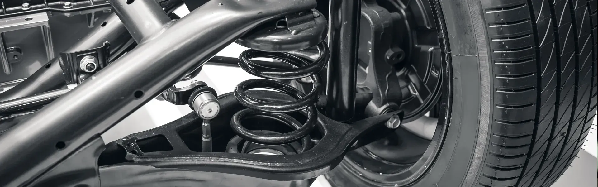 Close-up of a car’s rear suspension, coil spring, and tire under the chassis.