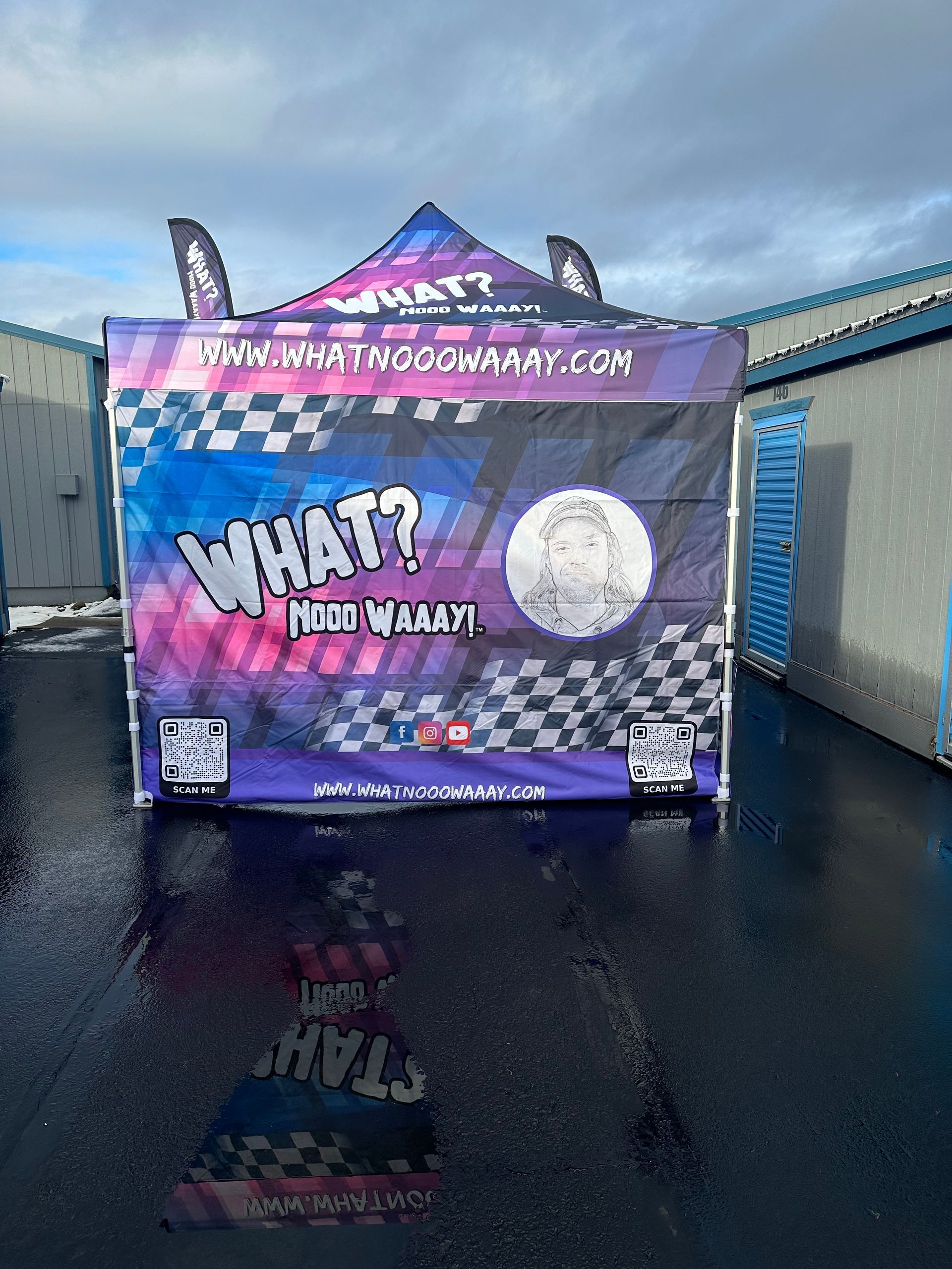 Purple event trailer with “WHAT?” graffiti-style text and checkered pattern on wet pavement