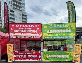 Two colorful fair food stands selling kettle corn and lemonade outdoors under a cloudy sky