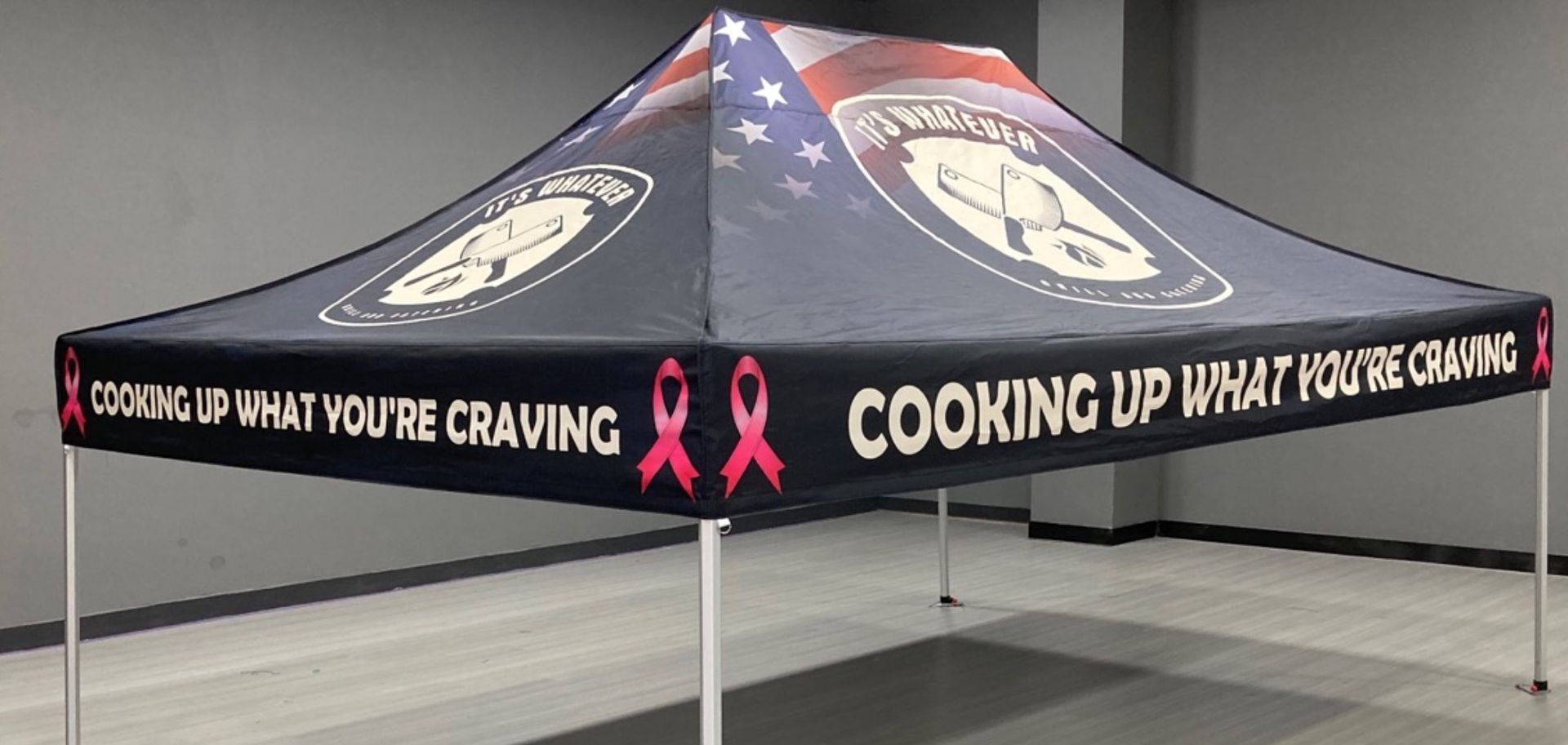 Black promotional canopy tent with pink ribbon graphics and “Cooking Up What You’re Craving” text indoors