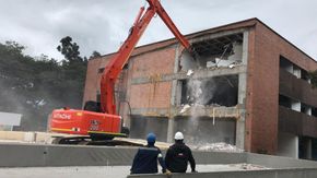 Una gran excavadora naranja está demoliendo un edificio de ladrillos.