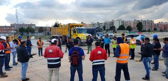 Un grupo de trabajadores de la construcción están parados en círculo frente a un camión de volteo.