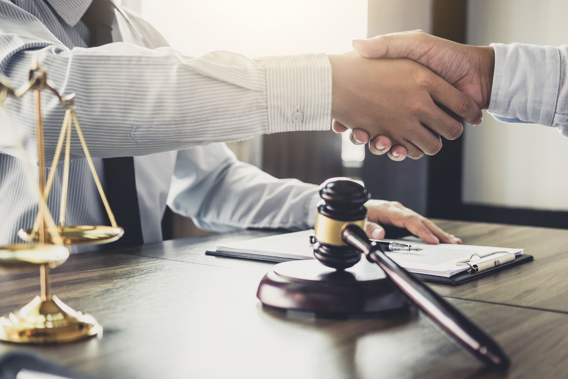 Handshake over legal desk with gavel, scales of justice, and a signed contract. Handshake over legal desk with gavel, scales of justice, and a signed contract.