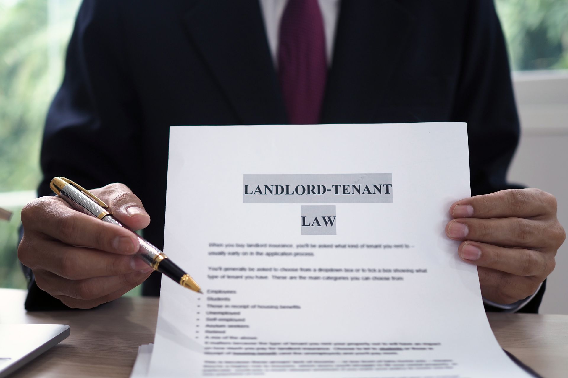 Person in suit holding a document titled “Landlord-Tenant Law” and a pen at a desk