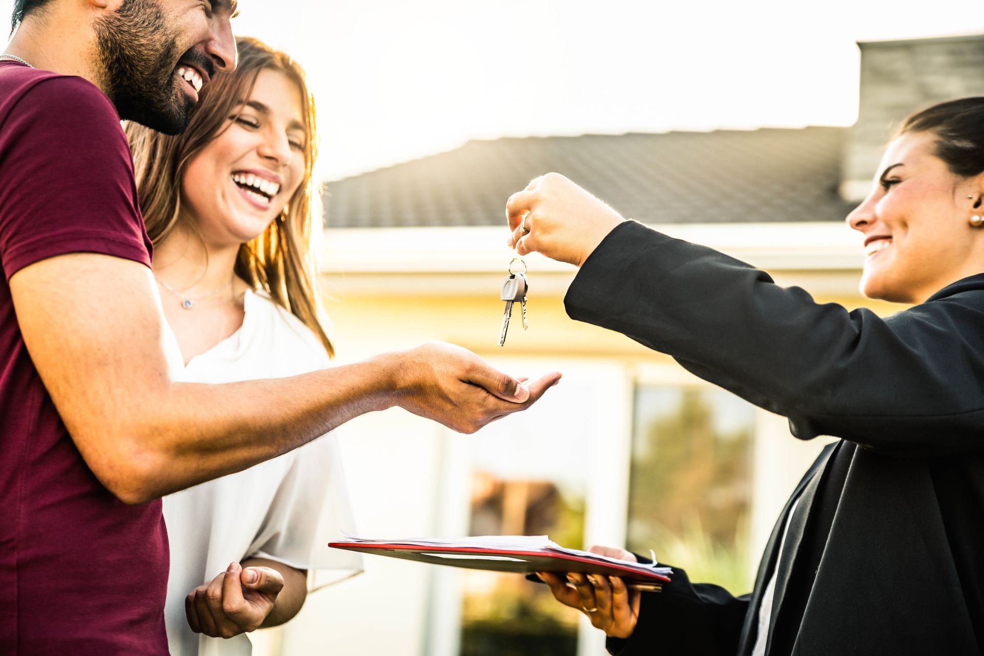 Two people receive house keys from a realtor outside a home, smiling during a home handoff. Two people receive house keys from a realtor outside a home, smiling during a home handoff.