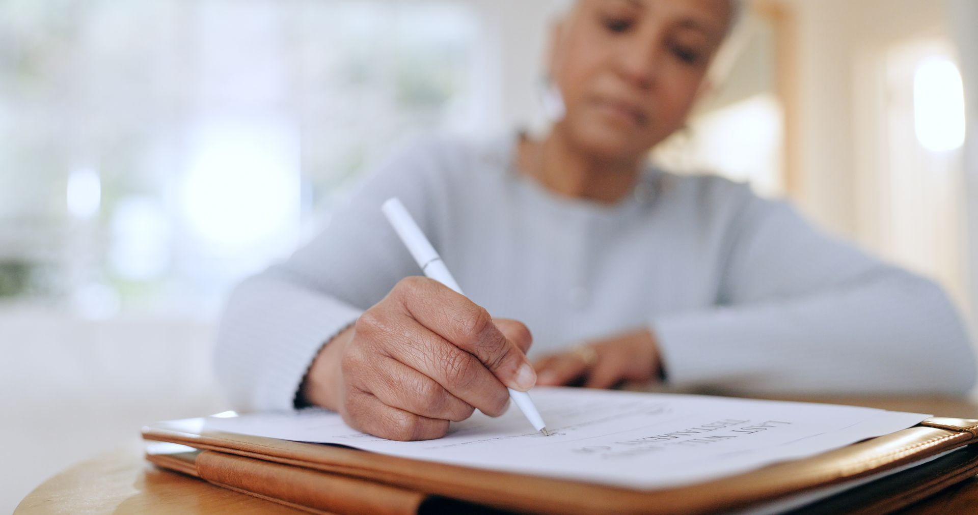 A person writing in a notebook at a table, with a blurred indoor background. A person writing in a notebook at a table, with a blurred indoor background.