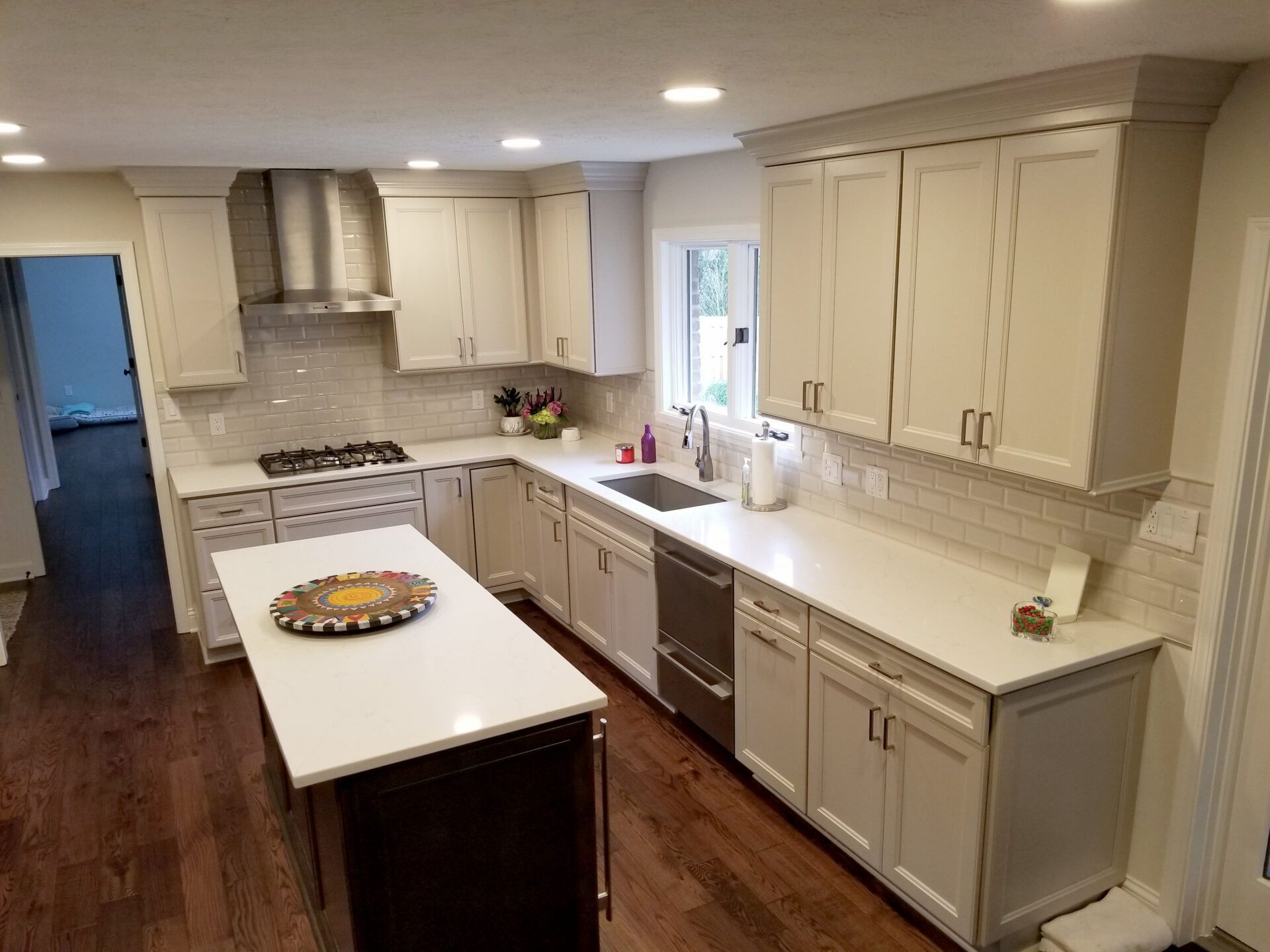 Modern kitchen with light gray cabinets, white countertops, and wood floors. Stainless steel appliances.
