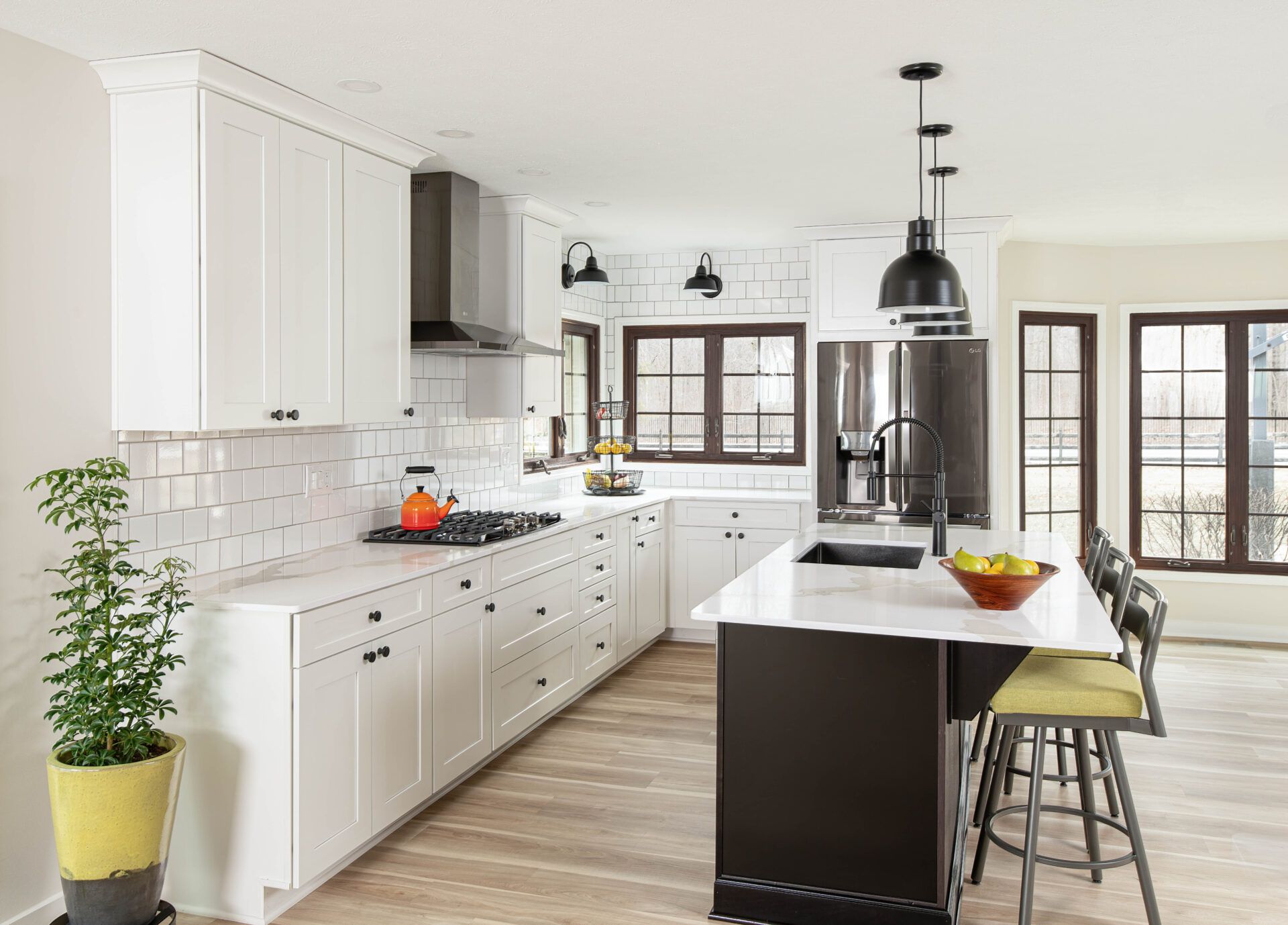 Modern white kitchen with dark island and brown window frames.