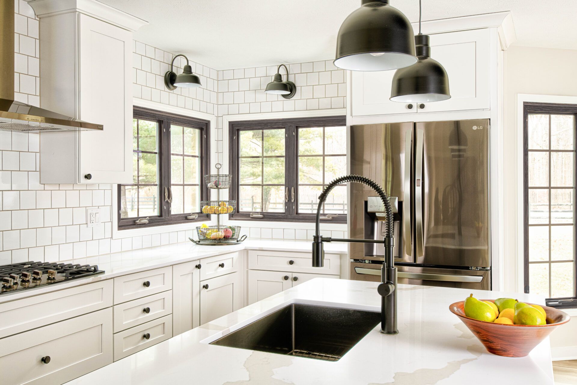 Modern white kitchen with black accents: cabinets, windows, faucet, and pendant lights.