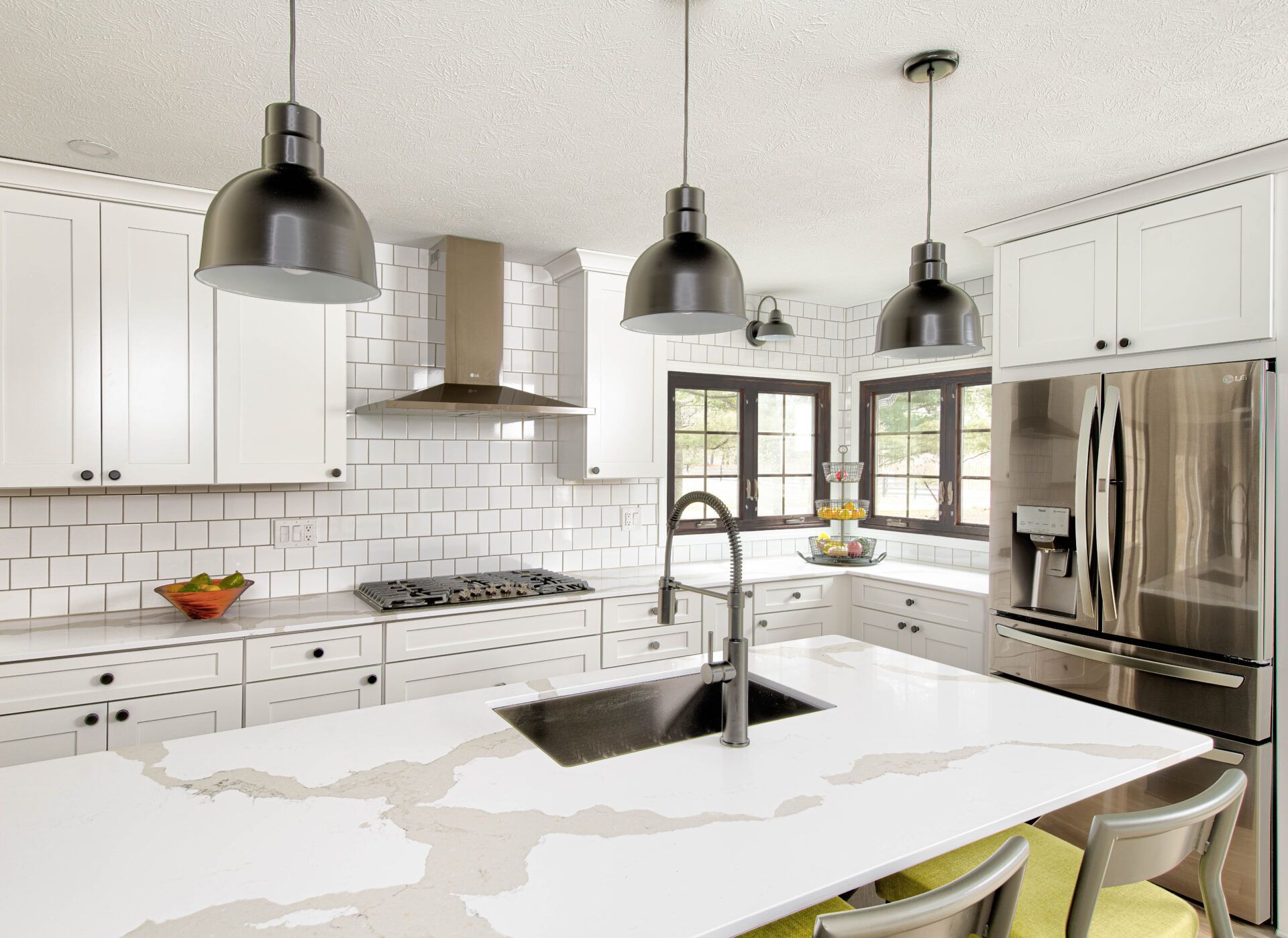Modern kitchen with white cabinets, island, and black pendant lights. Stainless steel refrigerator.