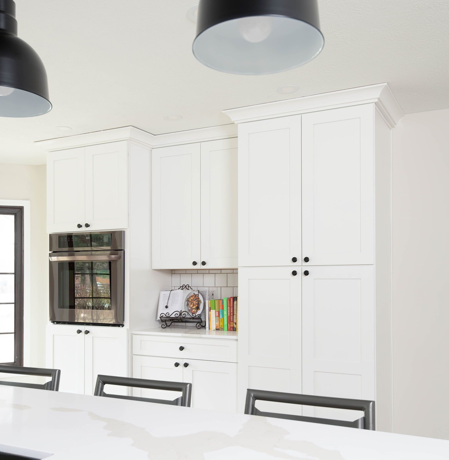 White kitchen cabinets with black hardware and pendant lights.