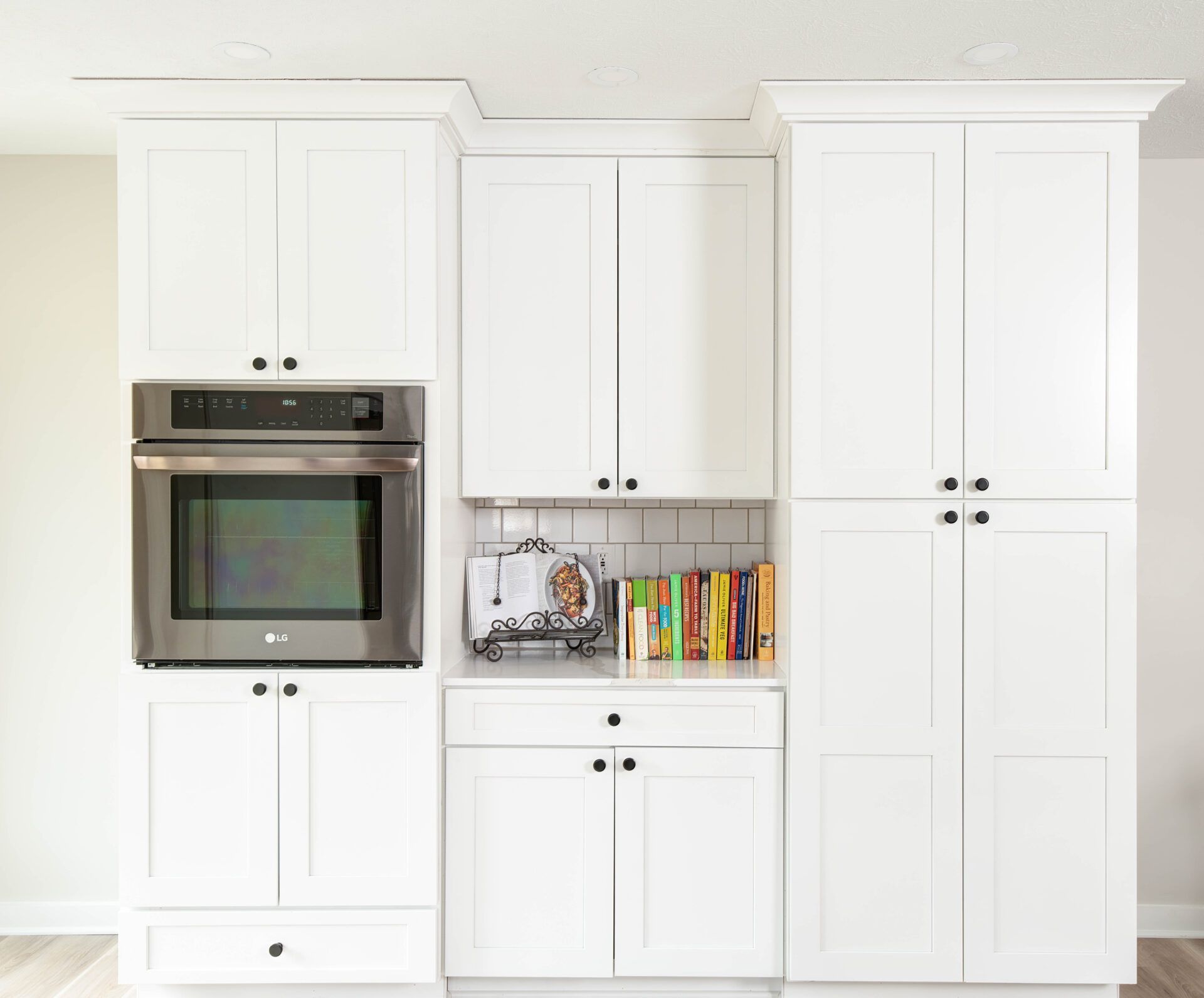 White kitchen cabinets with built-in oven and pantry; black hardware, books on counter.