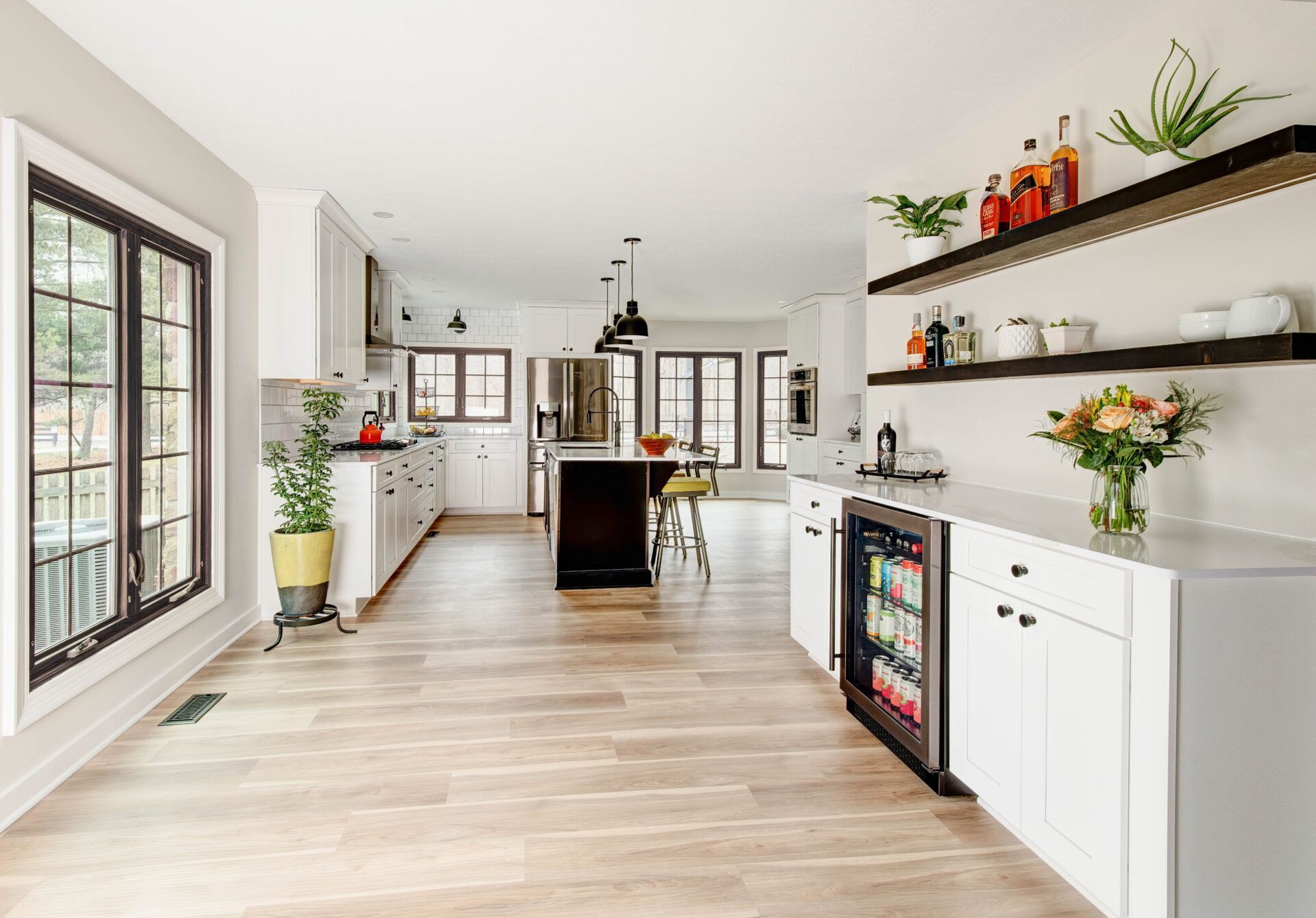 Modern kitchen with white cabinets, dark windows, and wood-look flooring. A built-in cooler and open shelving are visible.