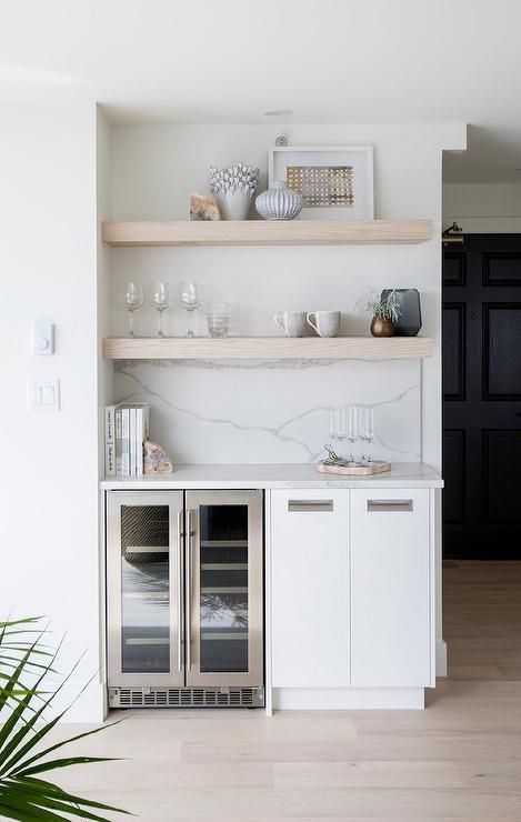 Built-in bar with shelves, a wine fridge, and white cabinets. Light wood shelves hold decor against a marble backsplash.