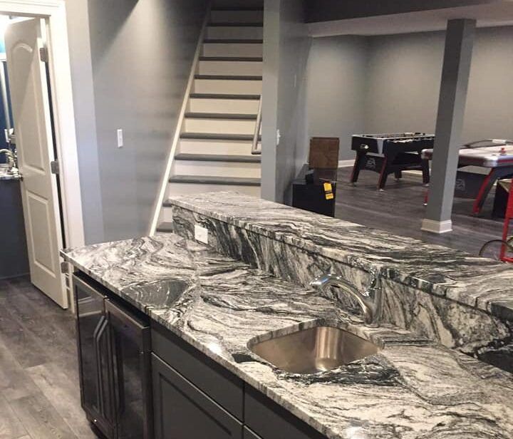 Granite countertop with sink and cabinets in a finished basement with stairs and a foosball table.