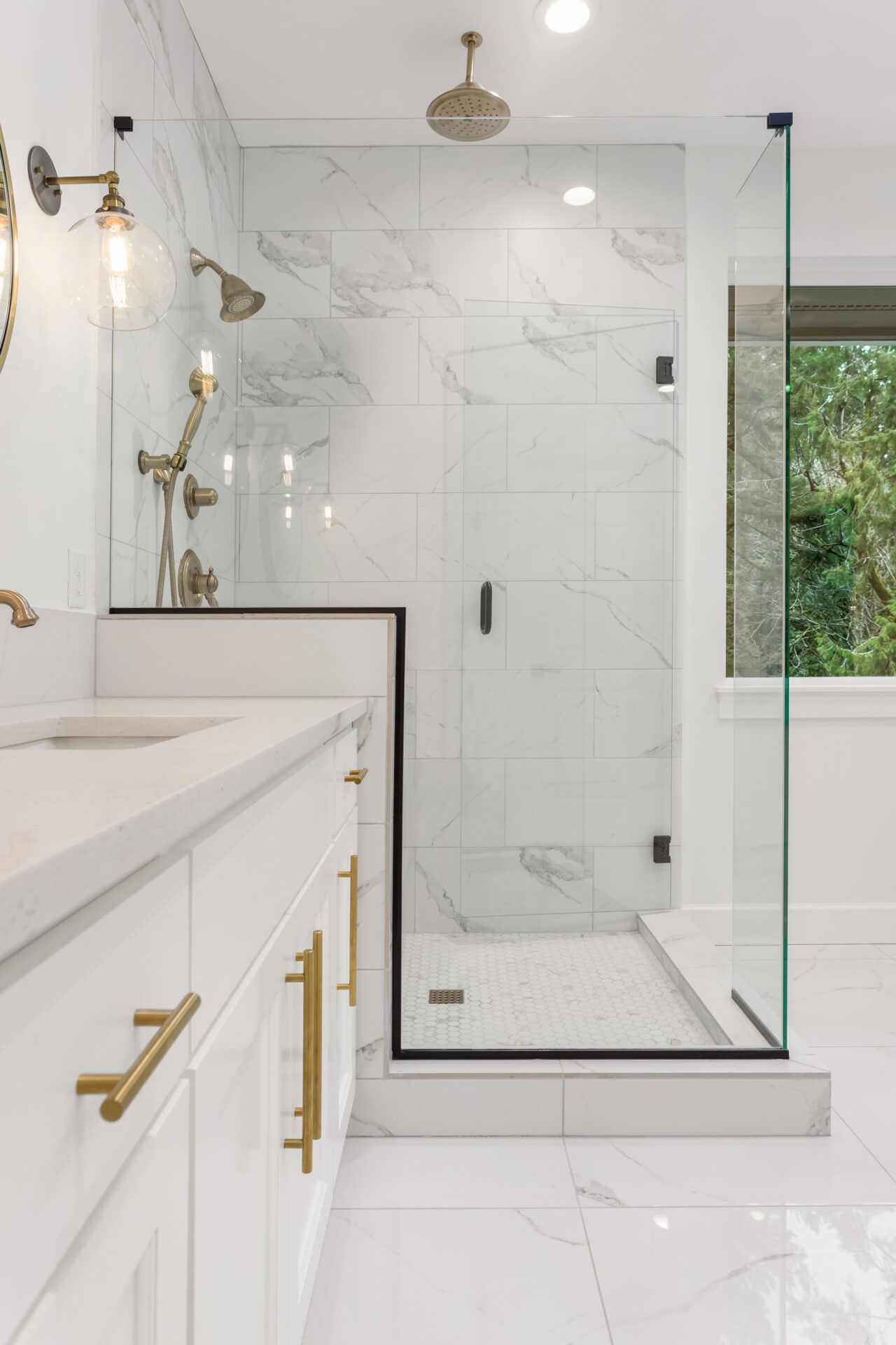 Modern white bathroom with marble tile shower, glass door, and gold fixtures.