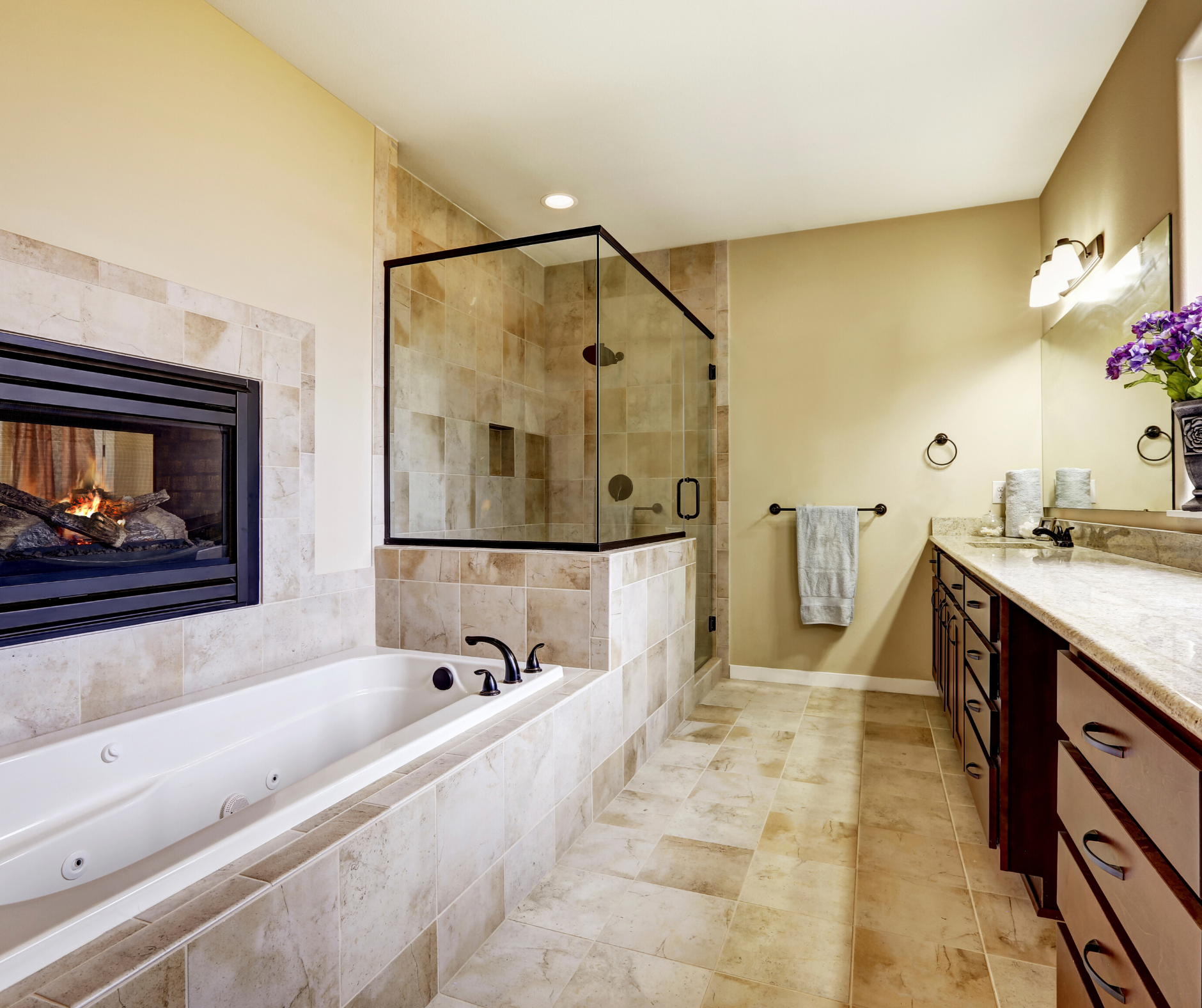 Bathroom with tiled walls and floor, a jacuzzi tub next to a fireplace, and a glass shower.