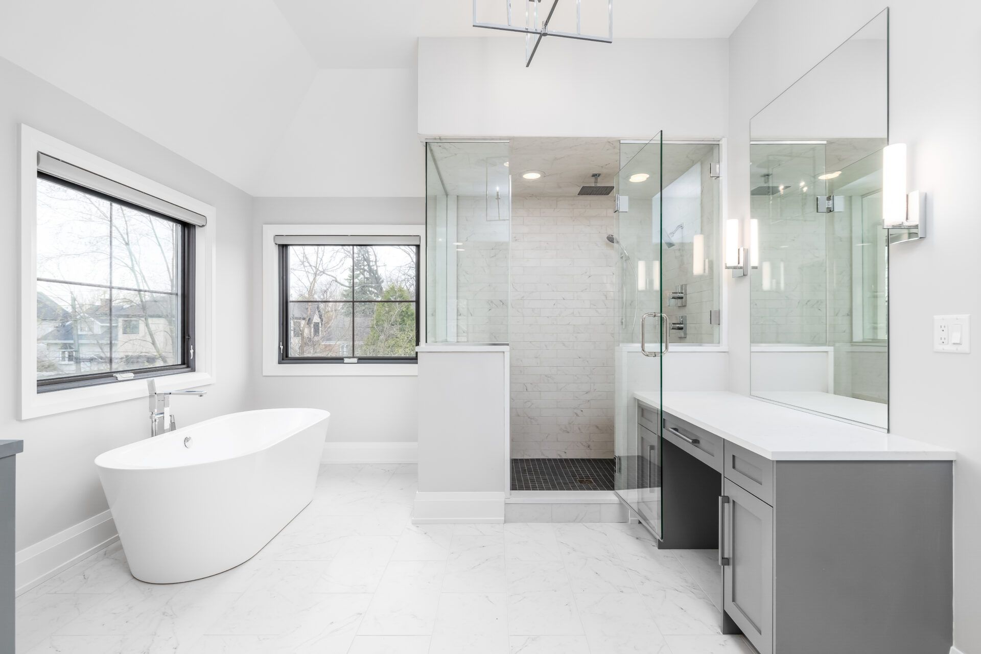 Spacious, modern bathroom with a freestanding tub, glass shower, and gray vanity; white walls and floor.