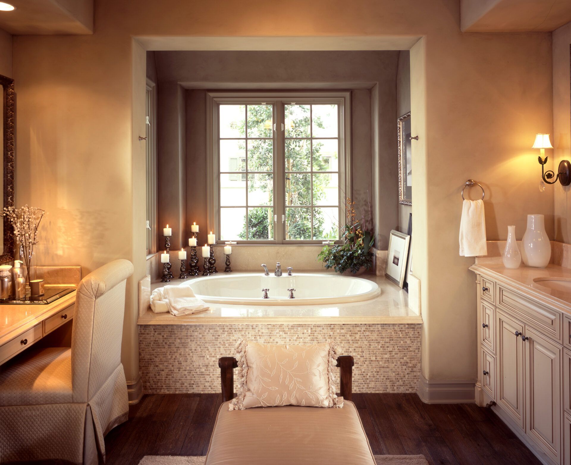 Bathroom with sunken bathtub, vanity, window with candles, beige and brown tones.