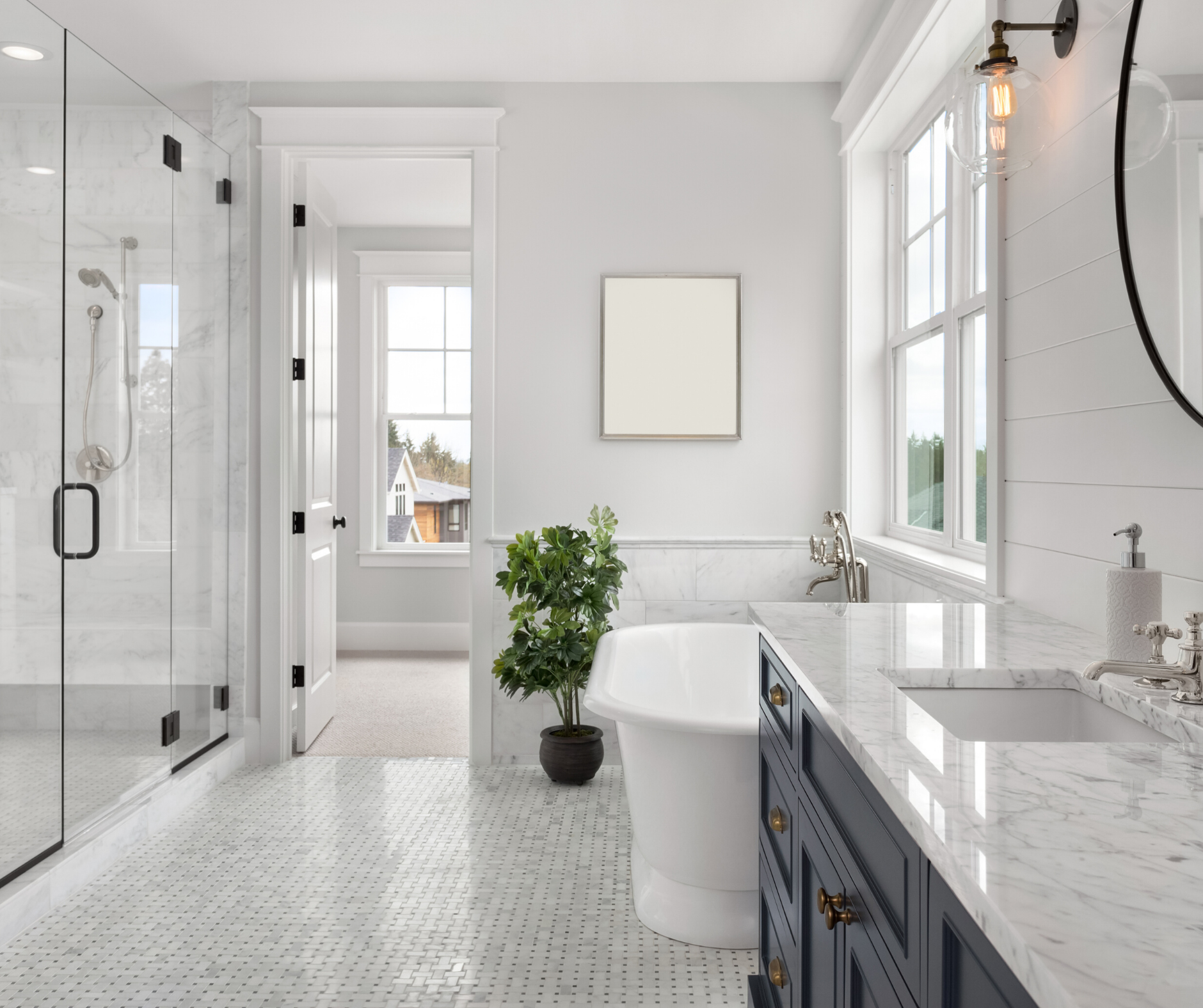 Bright bathroom with glass shower, white tub, dark blue vanity, and a framed light beige square on the wall.