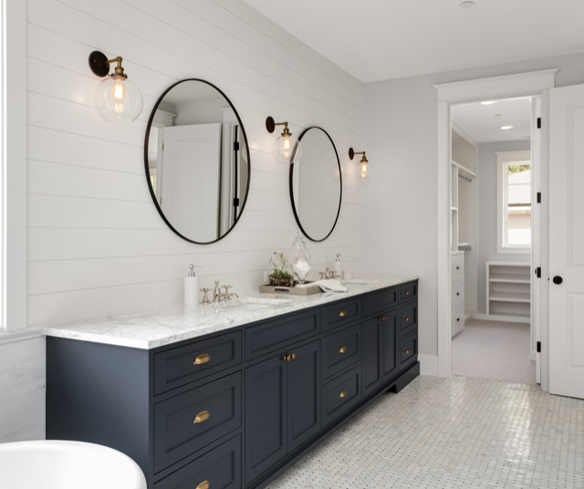 Modern bathroom with navy vanity, round mirrors, and glass sconces. Open doorway to a walk-in closet.