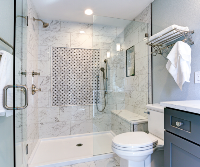 Modern shower with marble tiles, glass door, and built-in bench. White toilet next to shower.