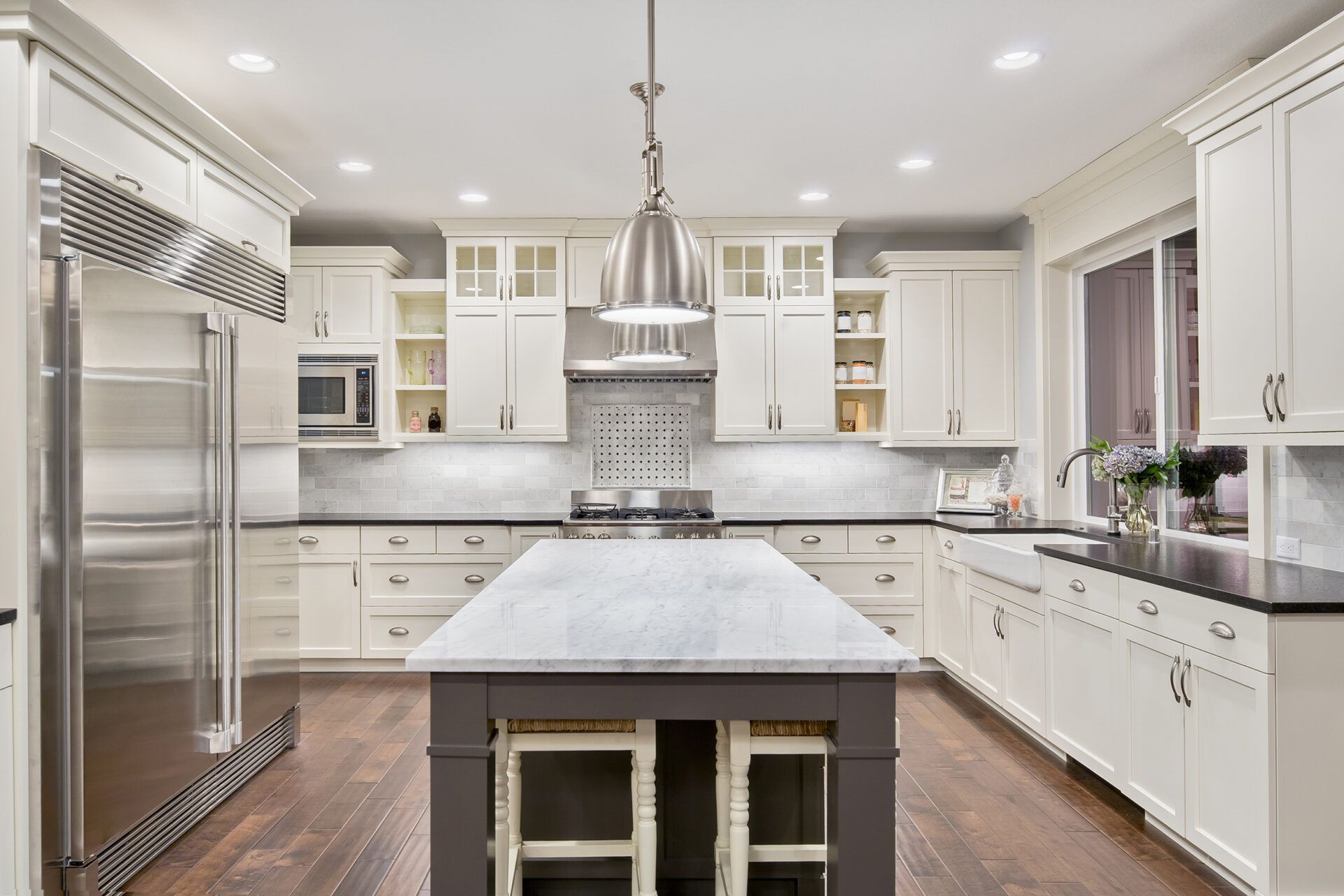 Bright white kitchen with island and stainless steel appliances; dark wood floor.