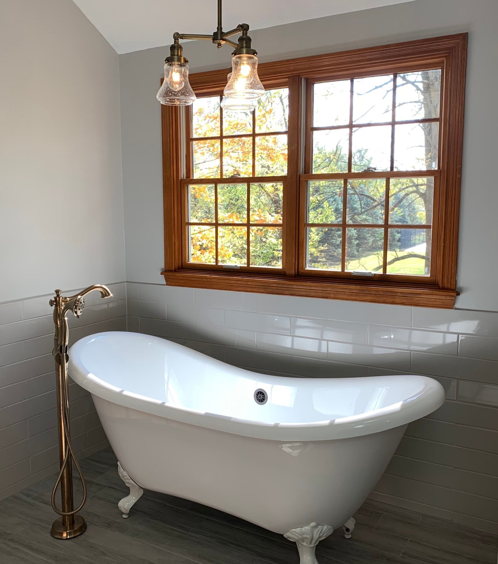 Bathroom with white clawfoot tub, gold fixtures, and a window with a view of fall foliage.