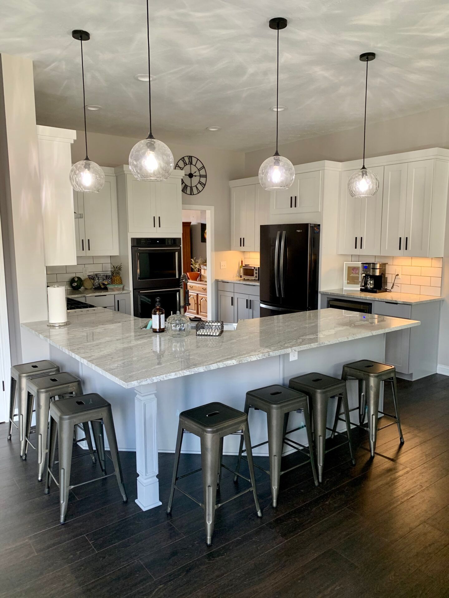 Kitchen with white cabinets, large island with gray stools, and pendant lights.