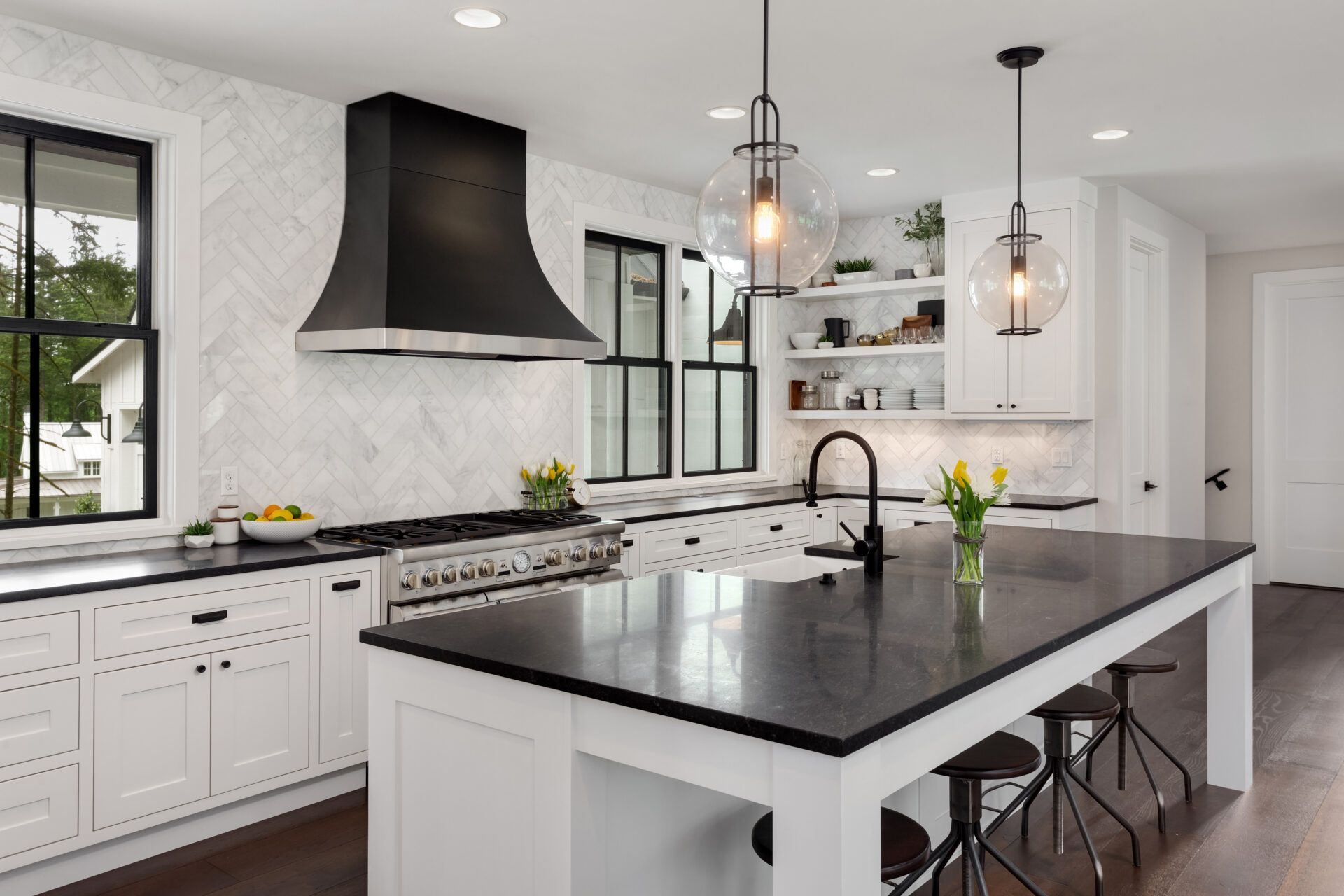 Modern white kitchen with black accents, island, range hood, and windows.