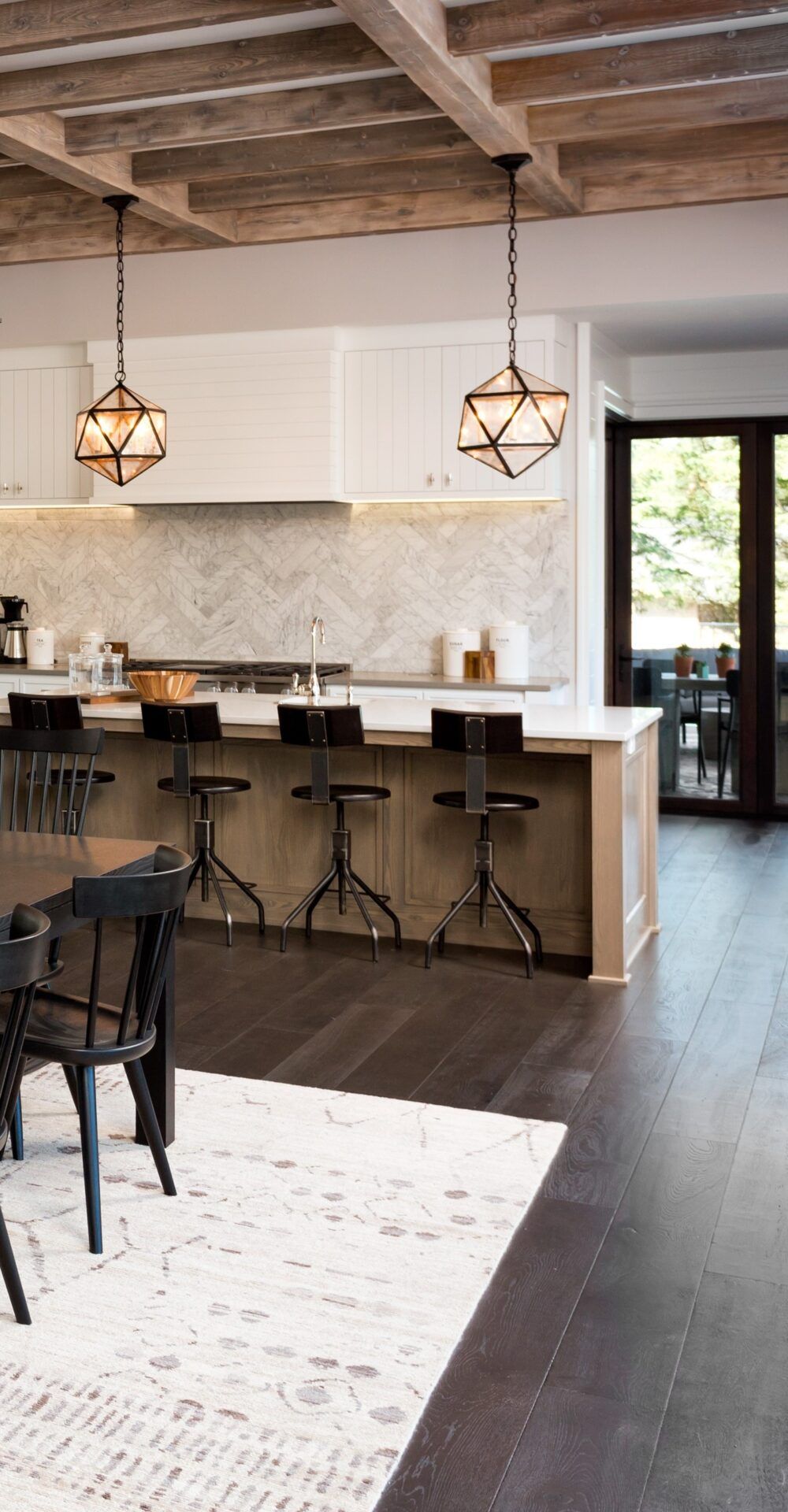 Kitchen with wooden beams, island with stools, patterned backsplash, and hanging lights.