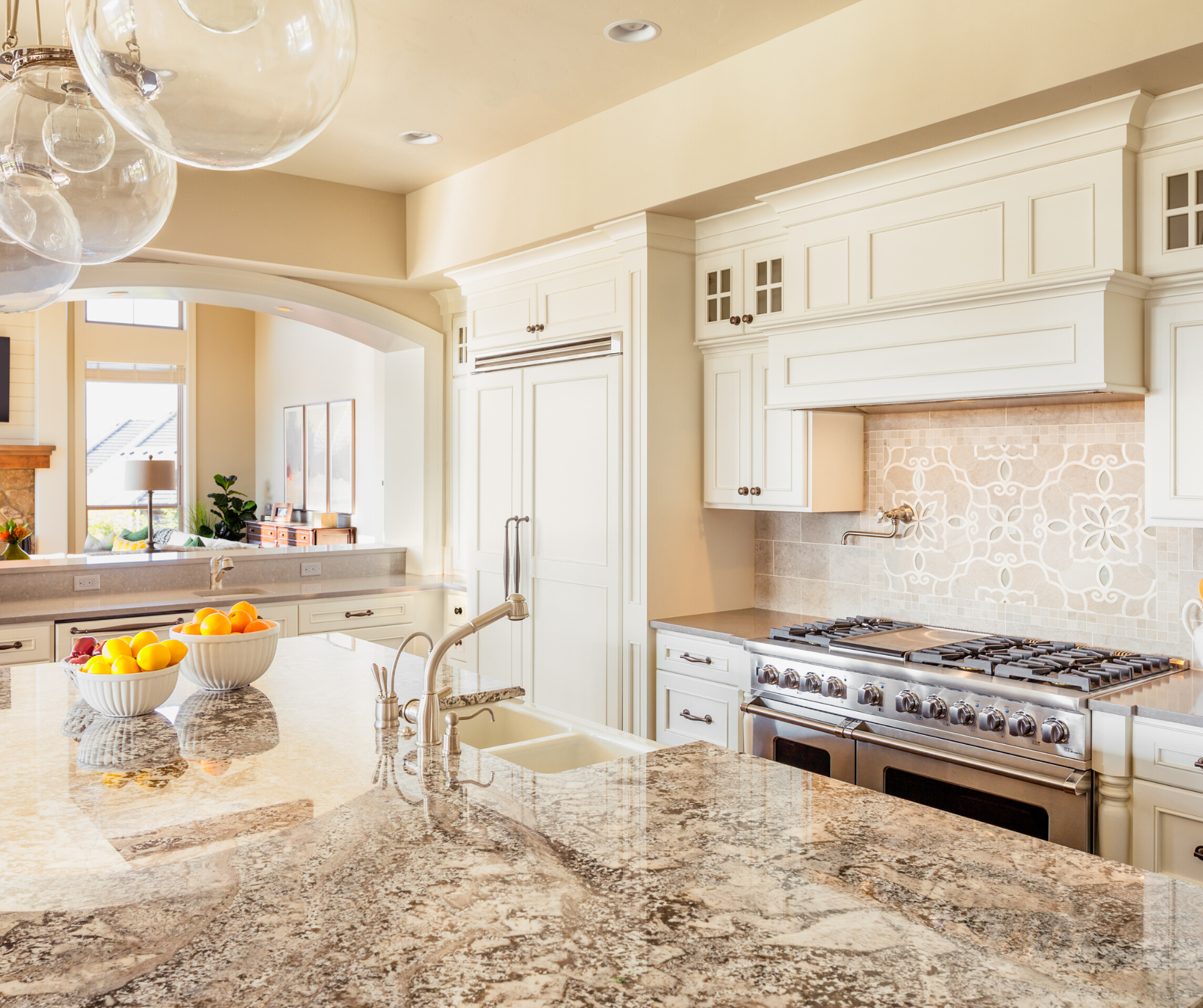 Elegant white kitchen with granite countertops, stainless steel appliances, and island with fruit.