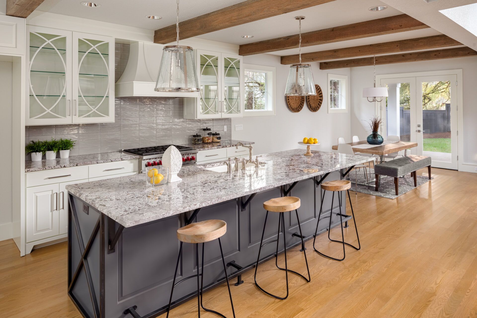 Modern kitchen with grey island, granite countertop, wooden stools, and white cabinets.
