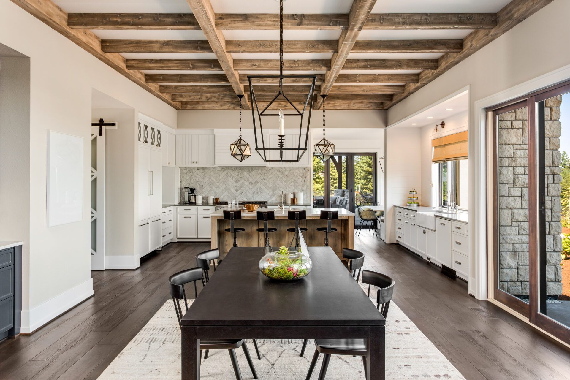 Dining room with dark table and chairs, white kitchen, wood ceiling beams, and sliding glass door.