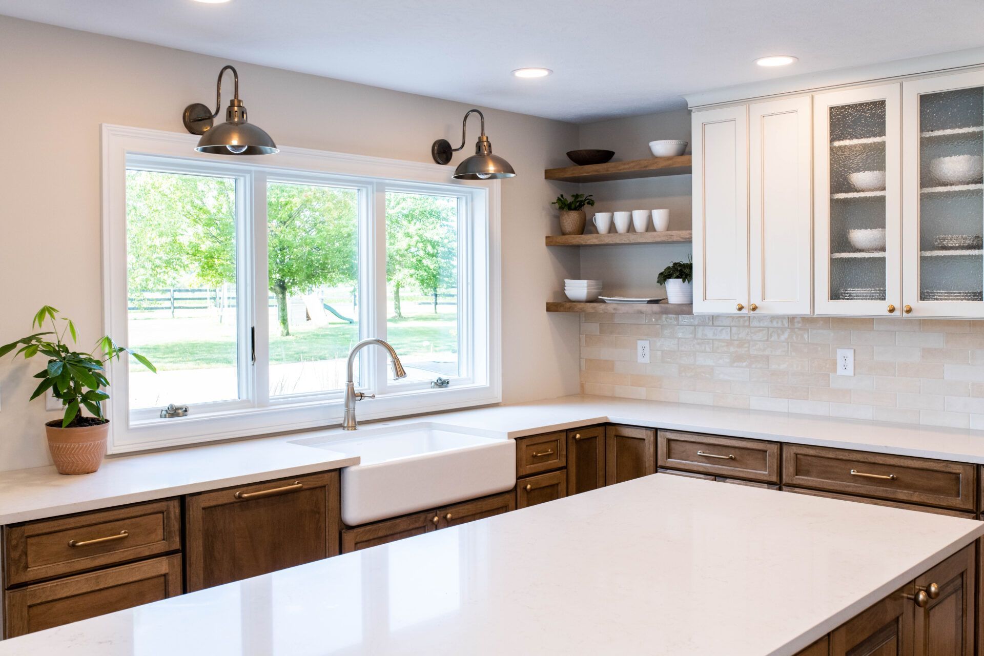 Kitchen with white countertops, brown cabinets, white farmhouse sink, and large window overlooking greenery.