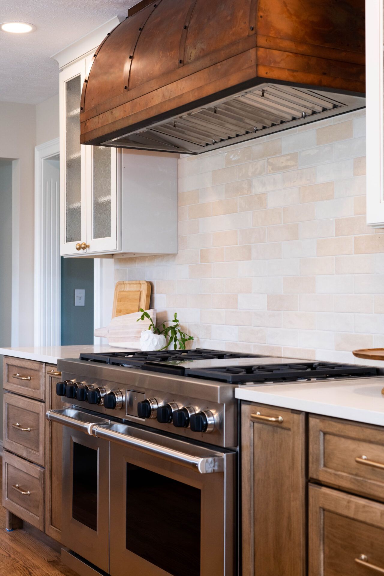 Kitchen with stainless steel range, wood hood, and light-colored tile backsplash.