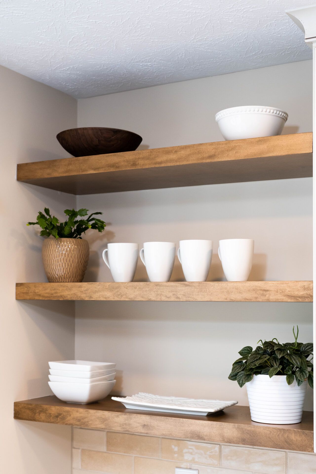 Wooden shelves in corner display bowls, mugs, and plants against a beige wall.